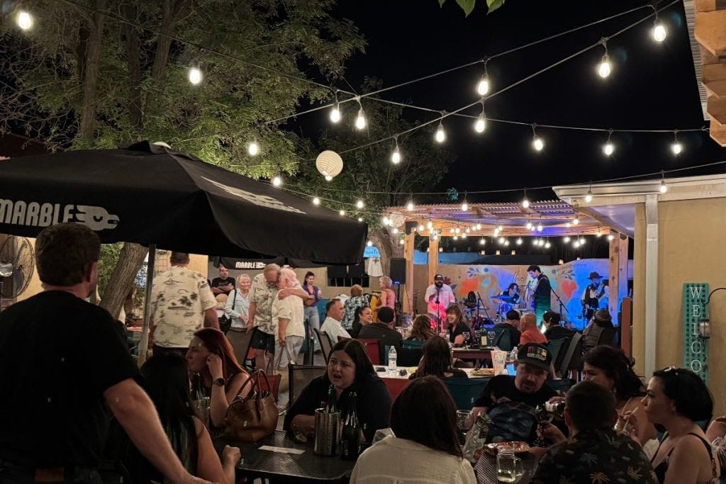 Outdoor restaurant patio in Las Cruces at night, where people dine under string lights and enjoy a live band performing on stage—a vibrant spot to experience local events.