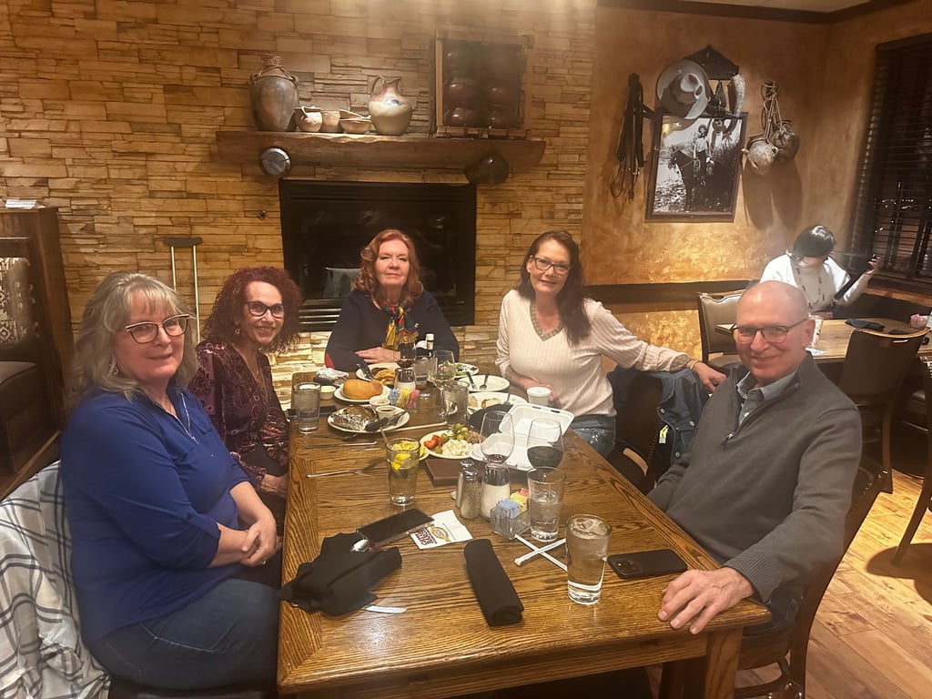 Live Love Las Cruces Launches Dinner Club to Spark Friendships and Community Connections 1 Five adults from a Dinner Club are seated around a restaurant table with food and drinks, posing for a group photo in a cozy, rustic Las Cruces setting.