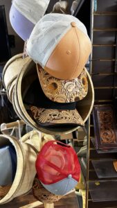 High Noon Leather trucker hats with tooled leather brims in orange, black, and red stacked on a shelf in Las Cruces, NM.