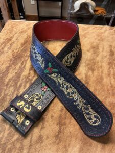 Black leather guitar strap by High Noon Leather with gold and red floral designs, red lining, and decorative stitching.