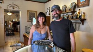 Smiling couple behind jewelry display at Mesilla shop in Las Cruces, NM, featuring authentic silver necklaces and rings.