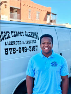 Smiling man in blue polo by Aggie Carpet Cleaning van displaying company info and phone number in Las Cruces, NM.