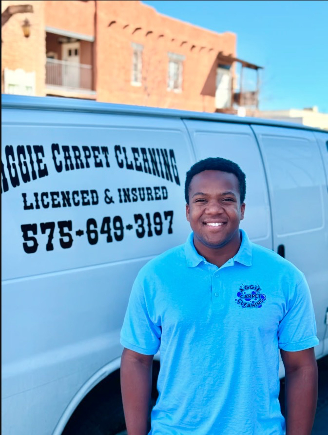 Smiling man in blue polo by Aggie Carpet Cleaning van displaying company info and phone number in Las Cruces, NM.